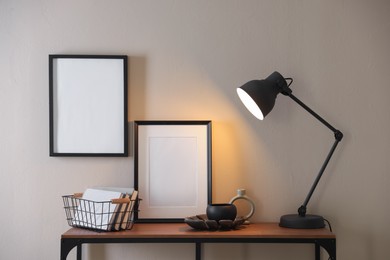 Photo of Stylish lamp, other decor and books on console table near beige wall indoors