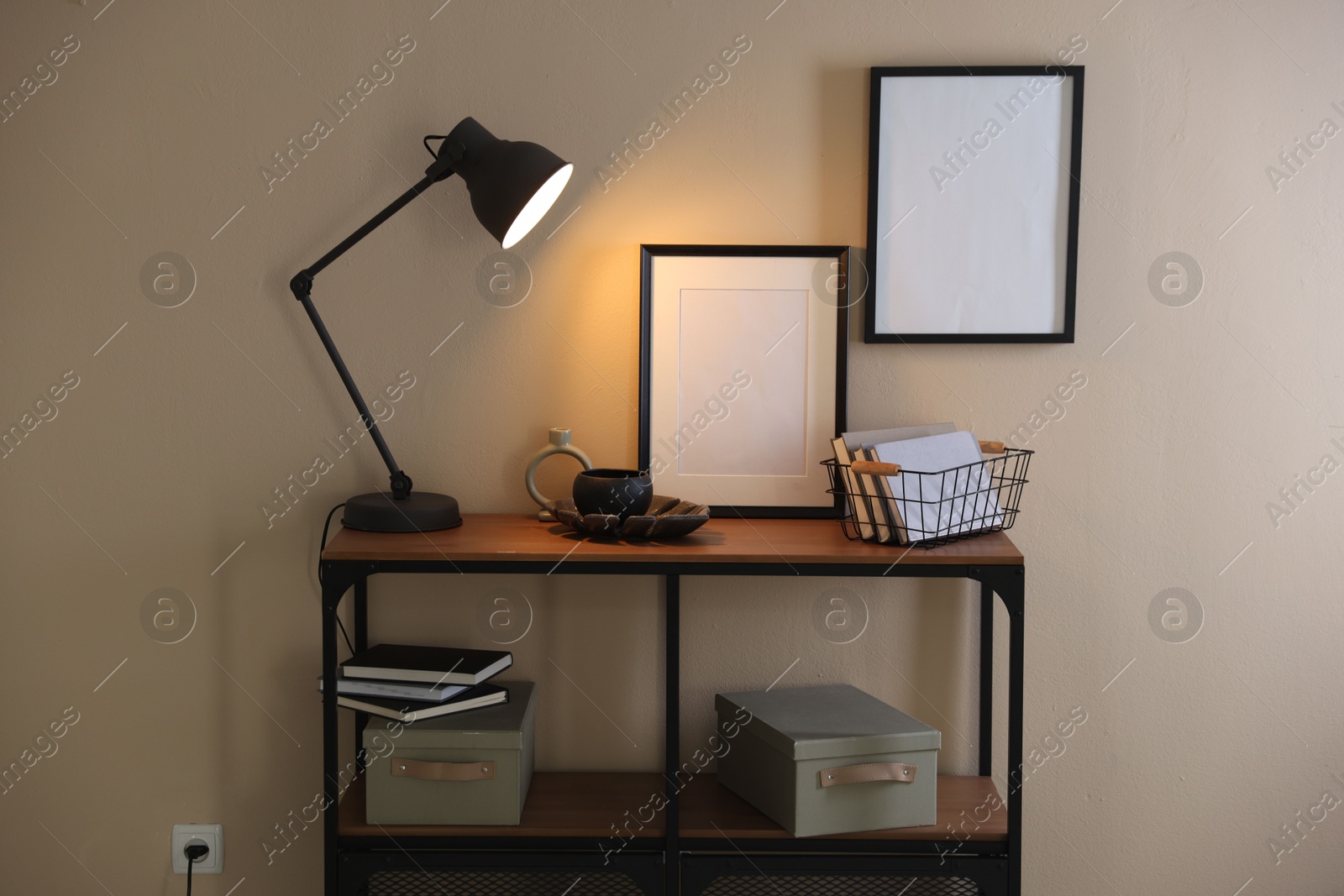 Photo of Stylish lamp, other decor and books on console table near beige wall indoors