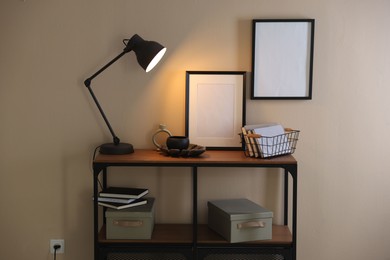 Photo of Stylish lamp, other decor and books on console table near beige wall indoors