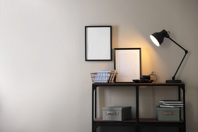 Photo of Stylish lamp, other decor and books on console table near beige wall indoors, space for text