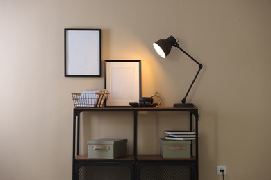 Photo of Stylish lamp, other decor and books on console table near beige wall indoors
