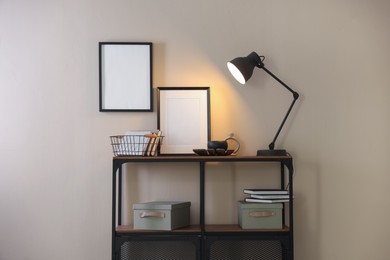 Photo of Stylish lamp, other decor and books on console table near beige wall indoors