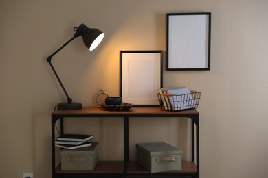 Photo of Stylish lamp, other decor and books on console table near beige wall indoors