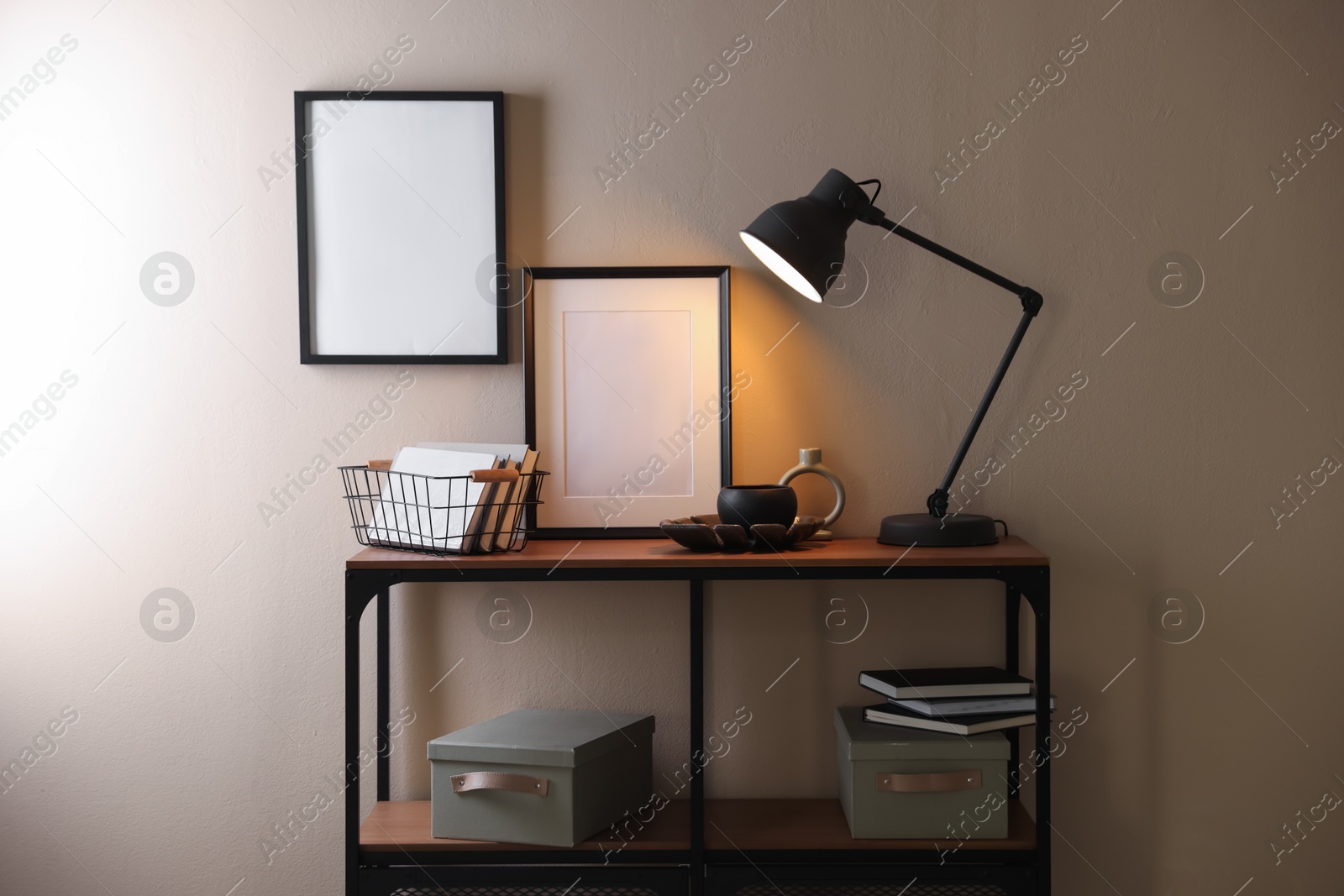 Photo of Stylish lamp, other decor and books on console table near beige wall indoors
