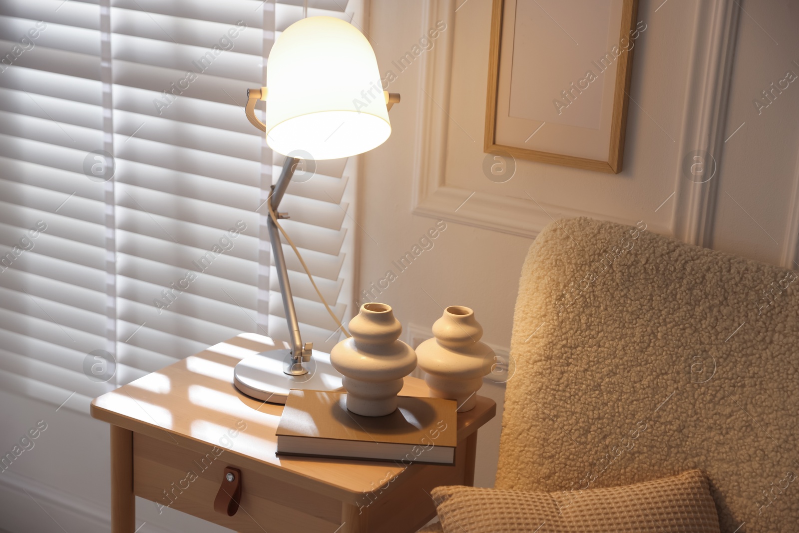 Photo of Stylish lamp, vases and book on wooden bedside table near armchair indoors