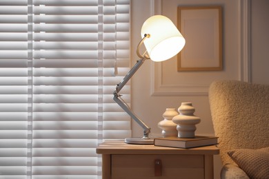 Photo of Stylish lamp, vases and book on wooden bedside table near armchair indoors, space for text