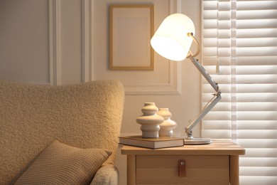 Photo of Stylish lamp, vases and book on wooden bedside table near armchair indoors