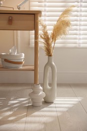 Photo of Stylish vases, dried reeds and bedside table near window indoors