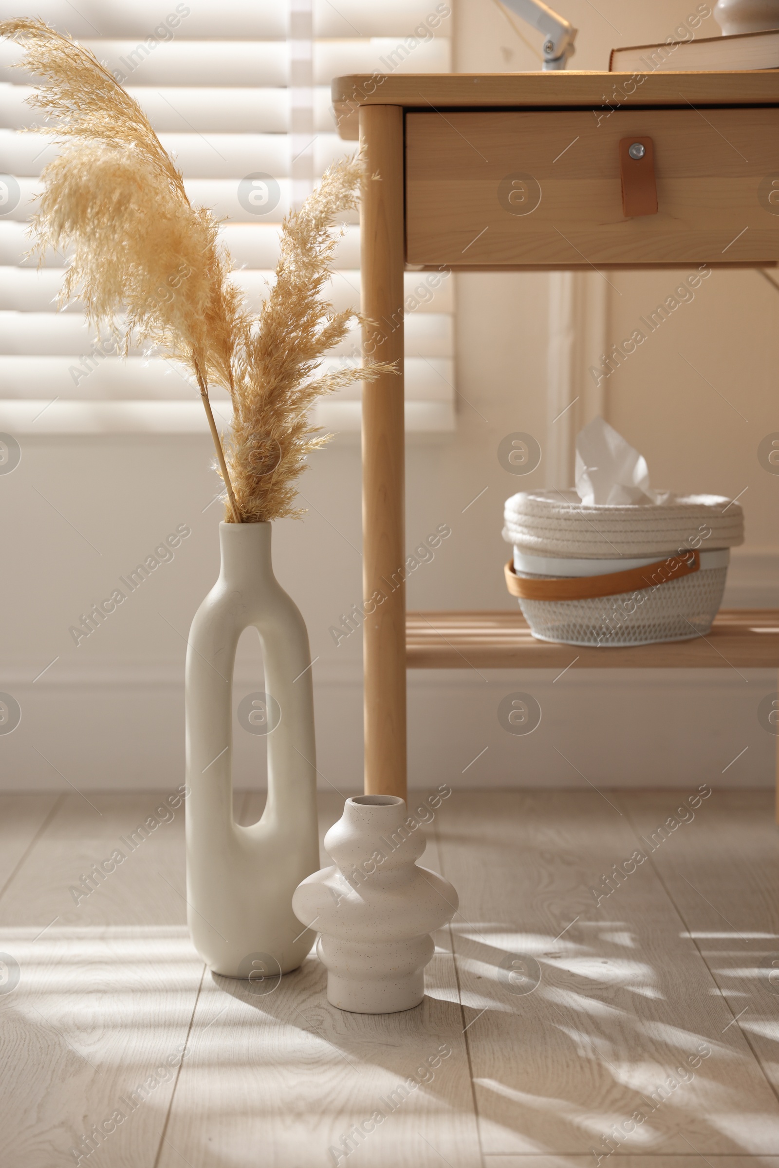 Photo of Stylish vases, dried reeds and bedside table near window indoors