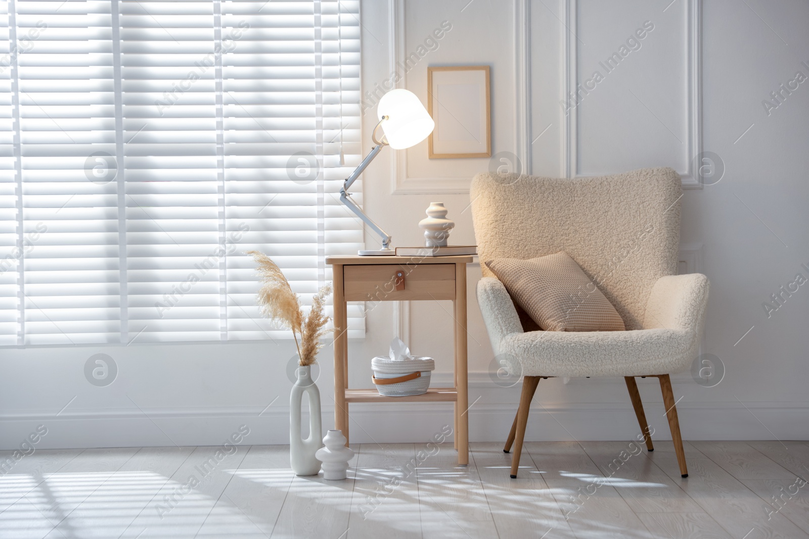 Photo of Stylish lamp, vase and book on wooden bedside table near armchair indoors, space for text
