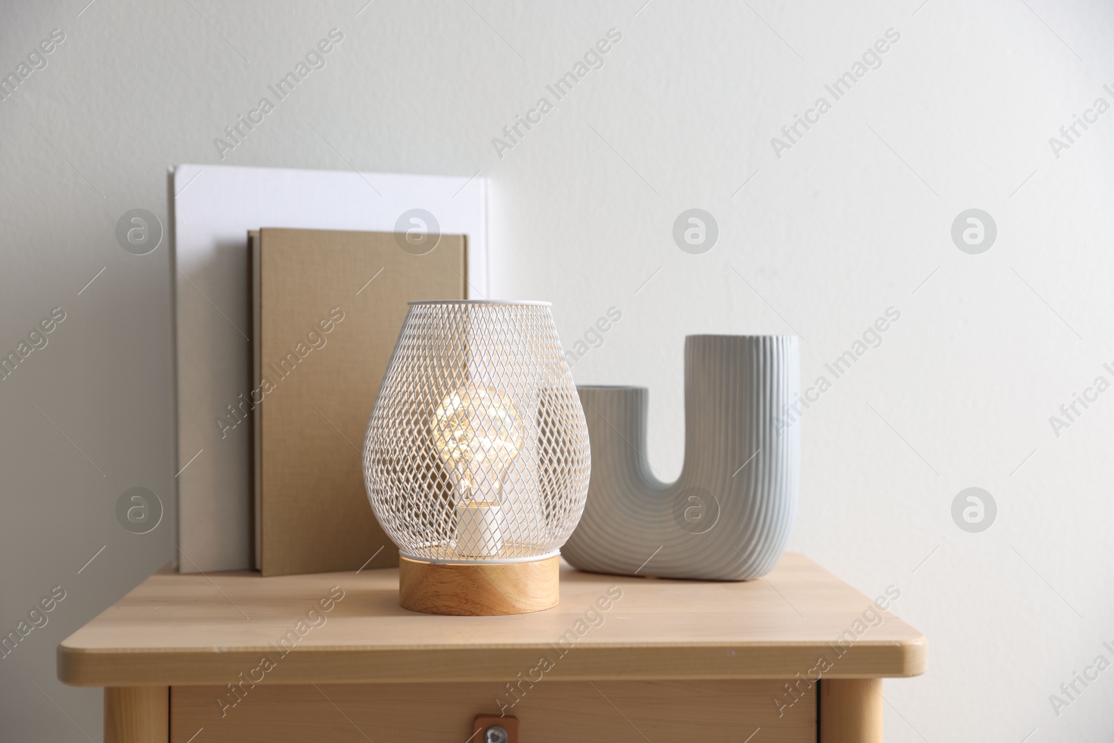 Photo of Stylish lamp, vase and books on wooden bedside table near white wall indoors