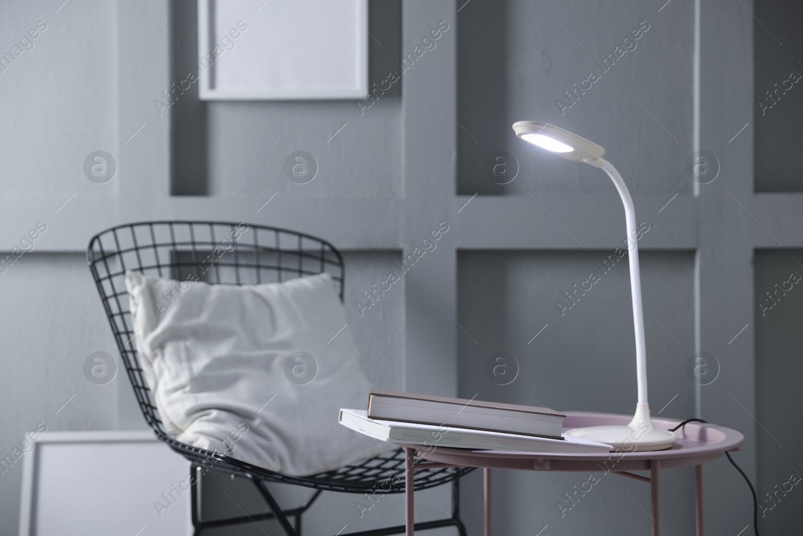 Photo of Stylish lamp and books on table near armchair indoors