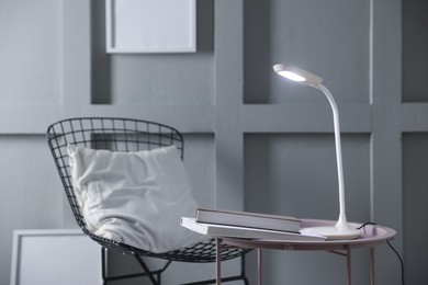 Photo of Stylish lamp and books on table near armchair indoors