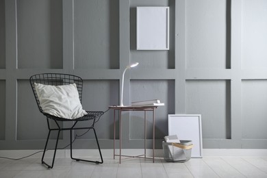 Photo of Stylish lamp and books on table near armchair indoors