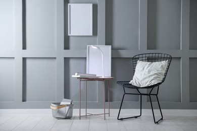 Photo of Stylish lamp and books on table near armchair indoors