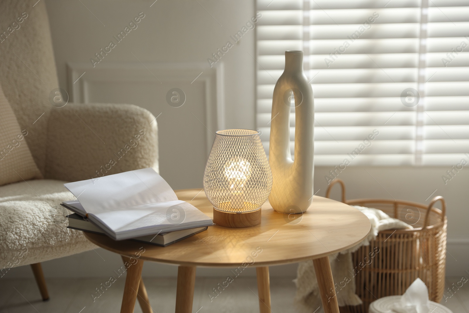 Photo of Stylish lamp, vase and books on wooden table near armchair indoors