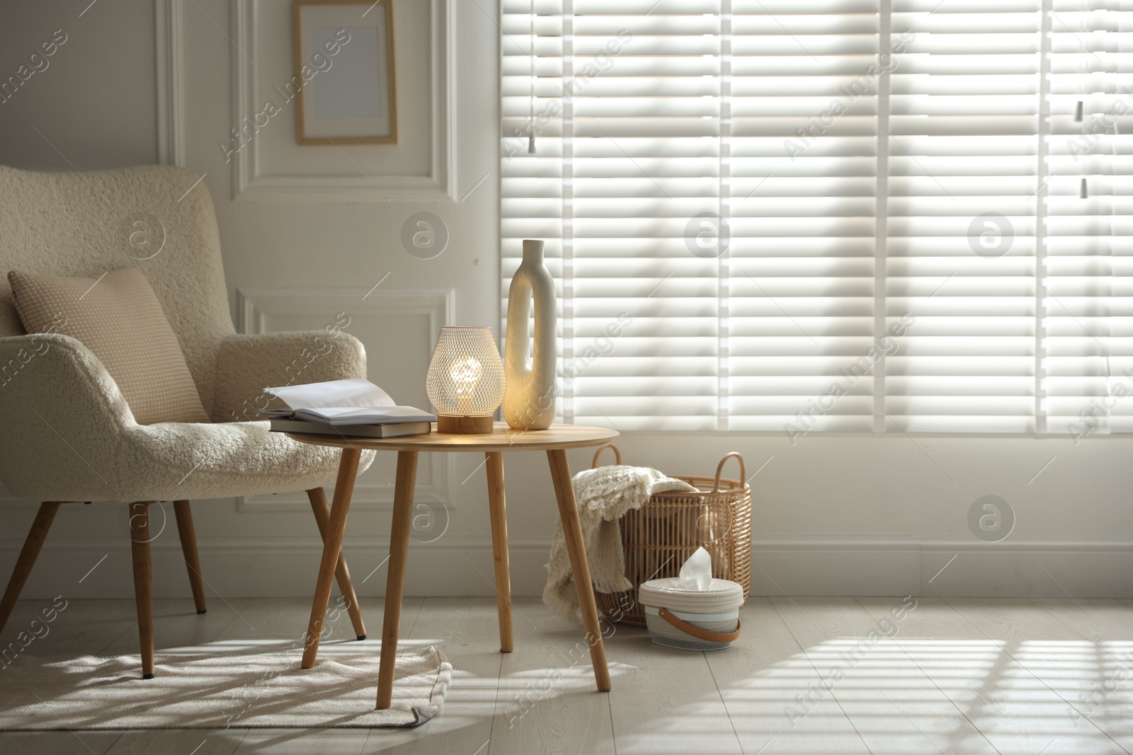 Photo of Stylish lamp, vase and books on wooden table near armchair indoors, space for text