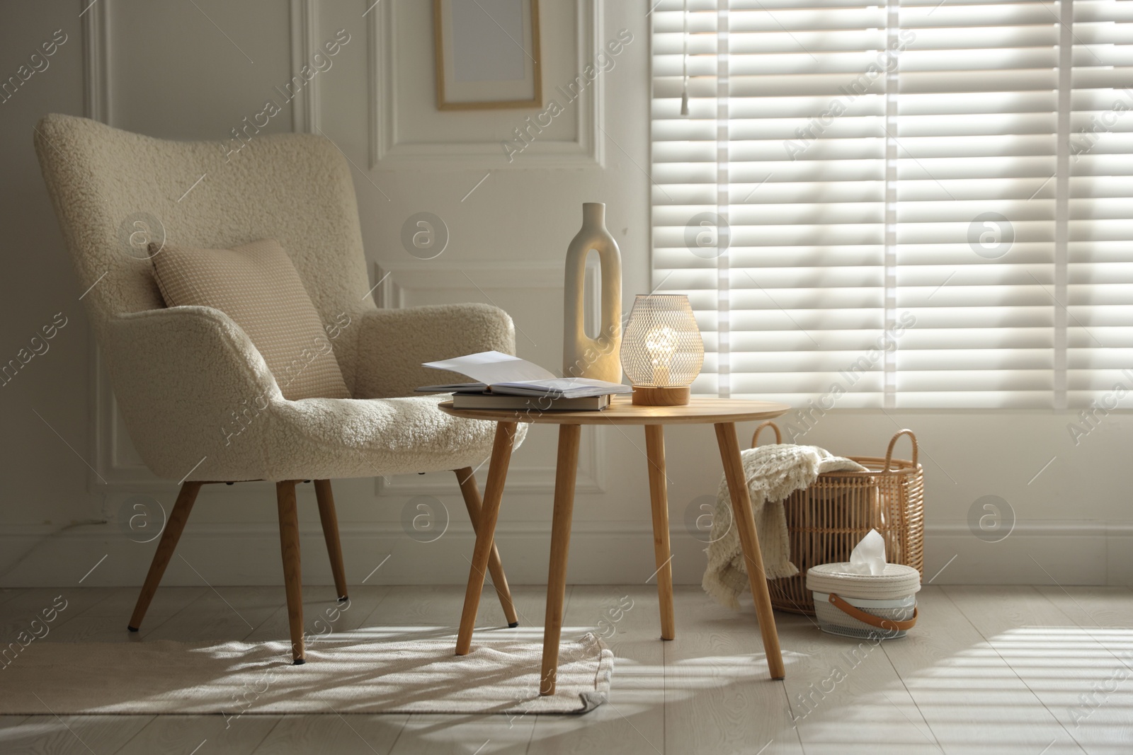 Photo of Stylish lamp, vase and books on wooden table near armchair indoors