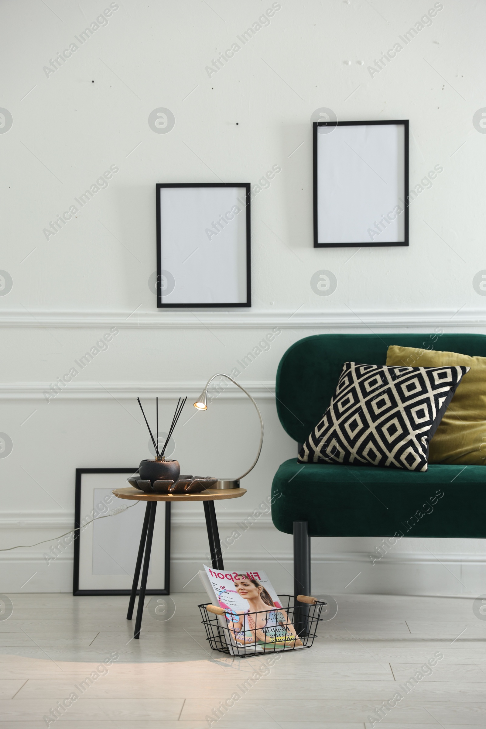 Photo of Stylish lamp, reed diffuser and magazine near armchair with pillows indoors