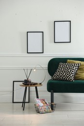 Photo of Stylish lamp, reed diffuser and magazine near armchair with pillows indoors
