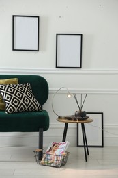 Photo of Stylish lamp, reed diffuser and magazine near armchair with pillows indoors