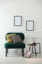Photo of Stylish lamp, reed diffuser and magazine near armchair with pillows indoors