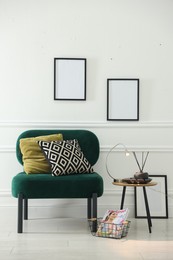 Photo of Stylish lamp, reed diffuser and magazine near armchair with pillows indoors