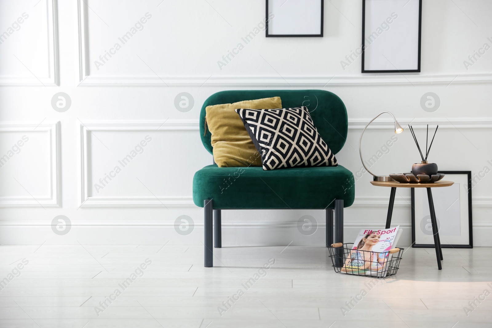 Photo of Stylish lamp, reed diffuser and magazine near armchair with pillows indoors, space for text