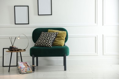 Photo of Stylish lamp, reed diffuser and magazine near armchair with pillows indoors, space for text