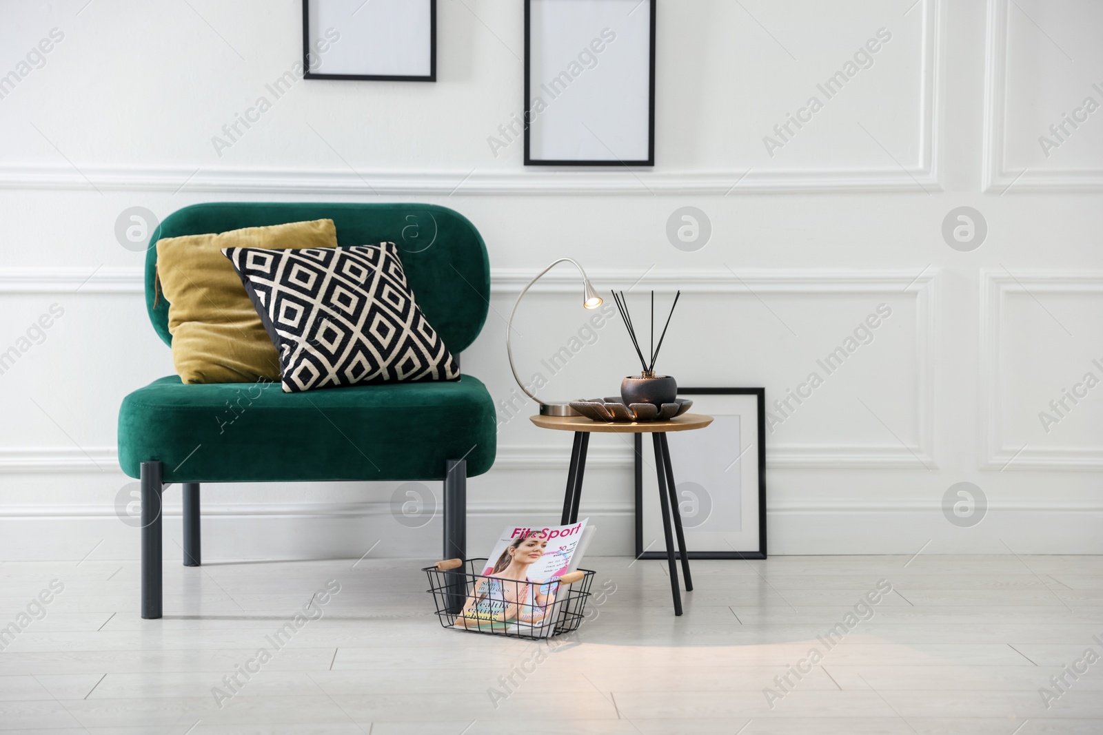 Photo of Stylish lamp, reed diffuser and magazine near armchair with pillows indoors, space for text