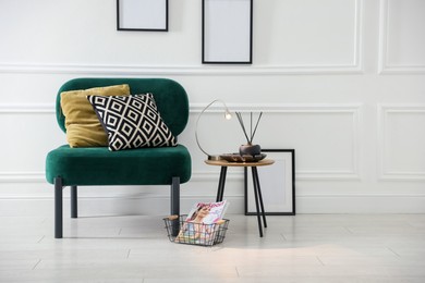 Photo of Stylish lamp, reed diffuser and magazine near armchair with pillows indoors, space for text