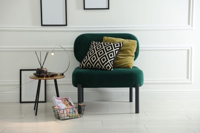 Photo of Stylish lamp, reed diffuser and magazine near armchair with pillows indoors
