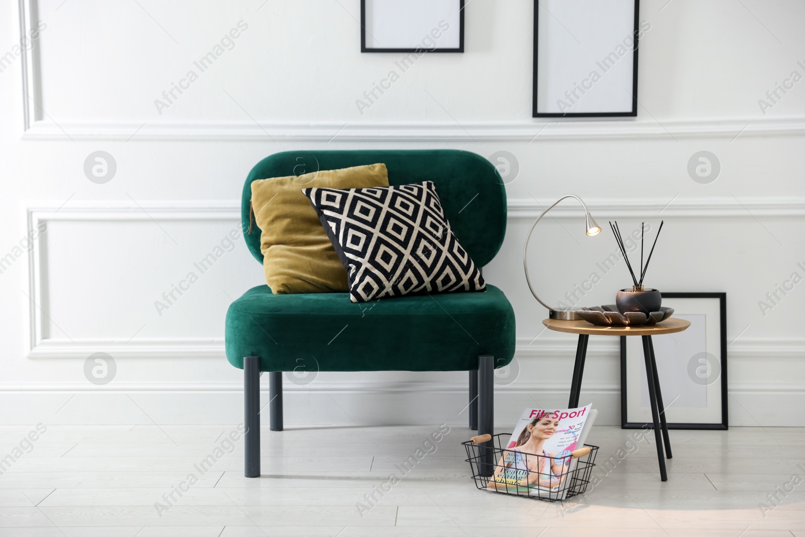Photo of Stylish lamp, reed diffuser and magazine near armchair with pillows indoors