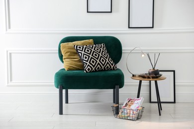 Photo of Stylish lamp, reed diffuser and magazine near armchair with pillows indoors
