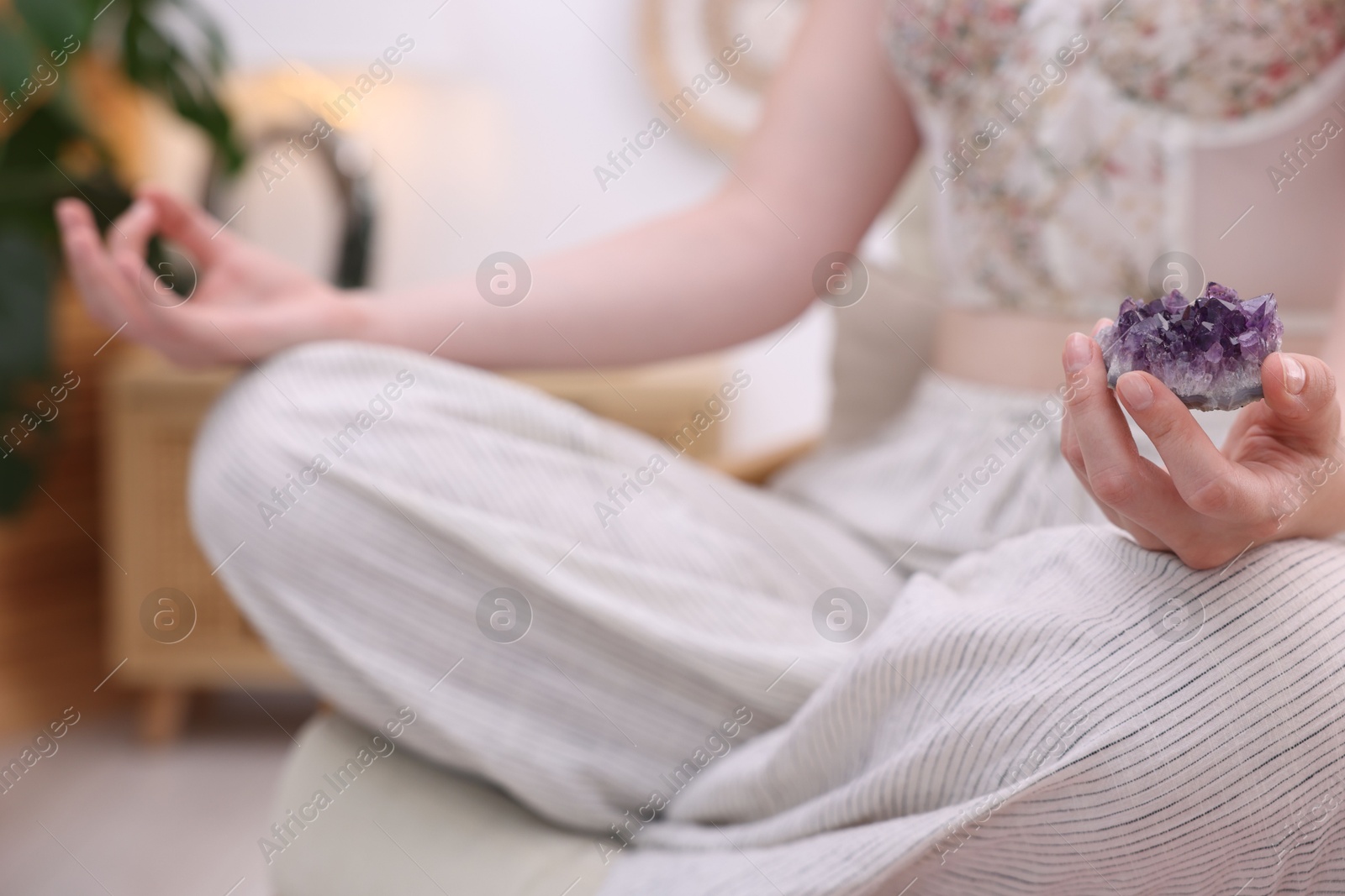 Photo of Woman with beautiful amethyst gemstone meditating indoors, closeup