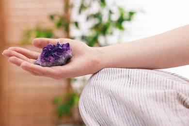 Photo of Woman with beautiful amethyst gemstone indoors, closeup