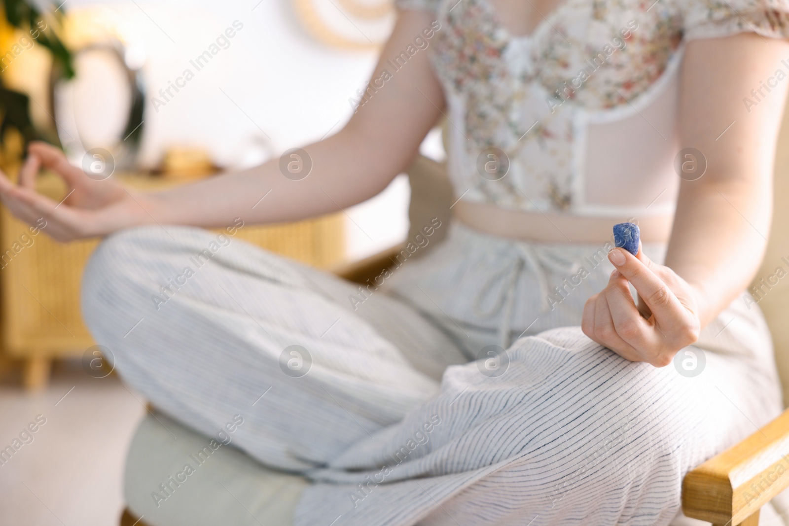Photo of Woman with blue sodalite gemstone meditating indoors, closeup