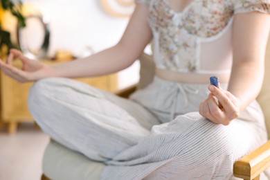 Photo of Woman with blue sodalite gemstone meditating indoors, closeup