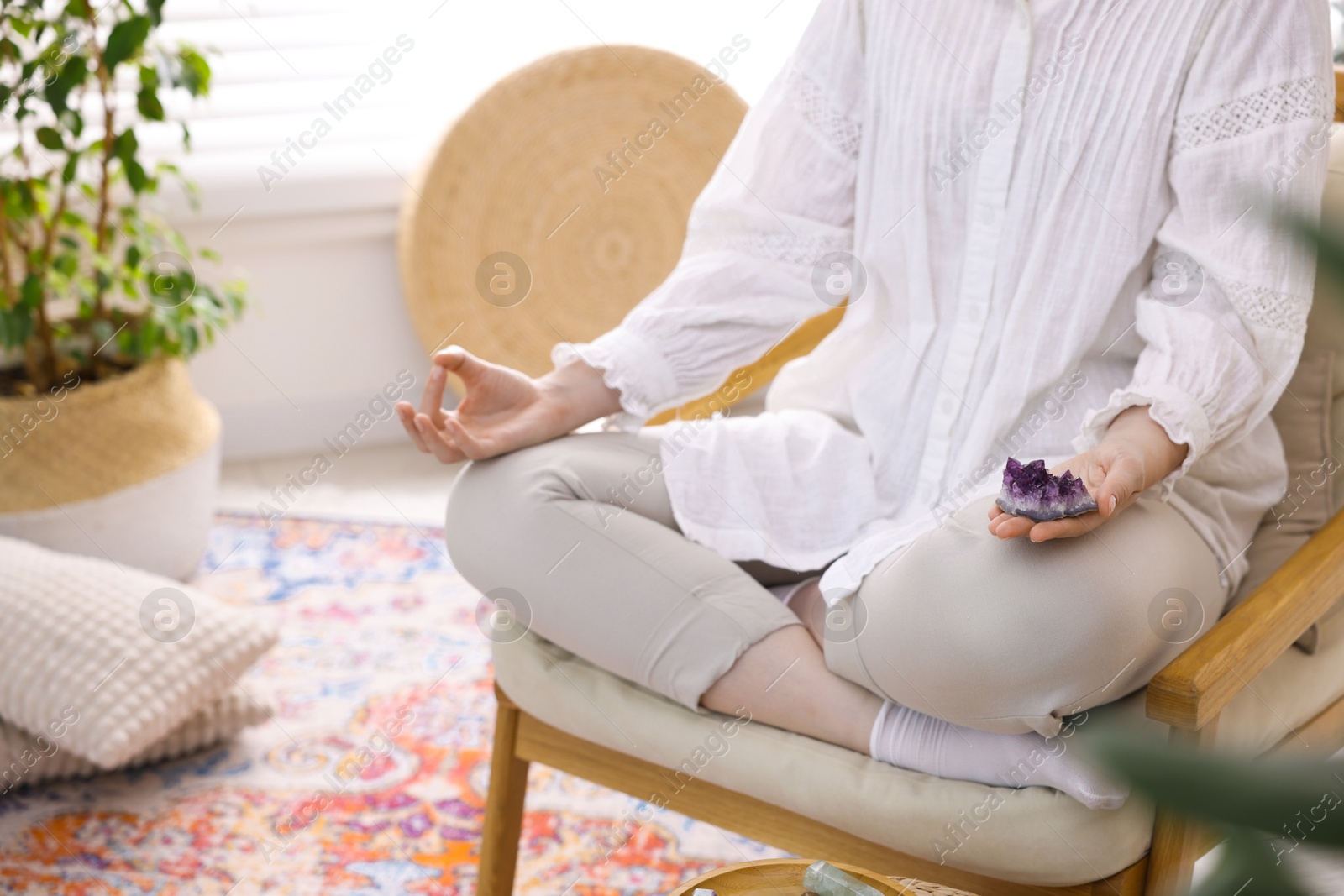 Photo of Woman with beautiful amethyst gemstone meditating indoors, closeup