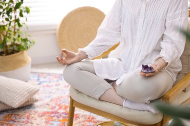 Photo of Woman with beautiful amethyst gemstone meditating indoors, closeup