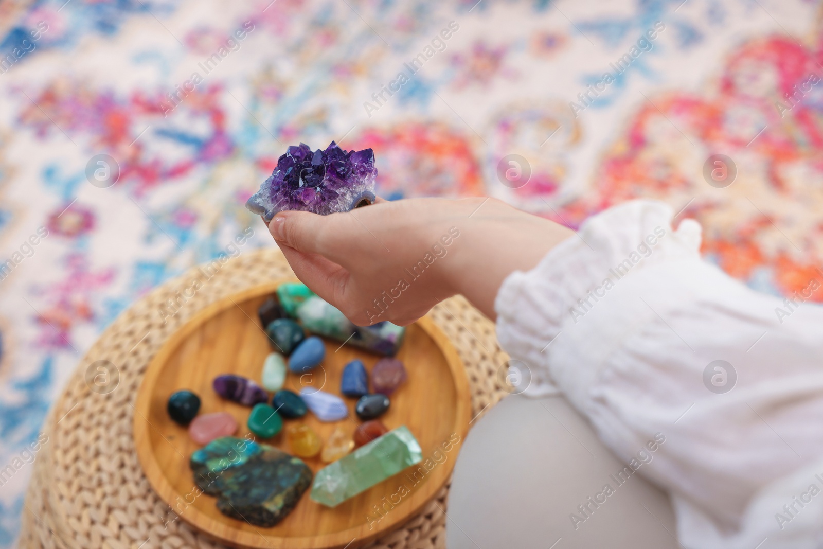 Photo of Woman with beautiful amethyst gemstone and other mineral stones indoors, closeup