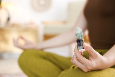 Photo of Woman with beautiful fluorite gemstone meditating indoors, closeup
