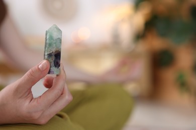 Photo of Woman with beautiful fluorite gemstone meditating indoors, closeup