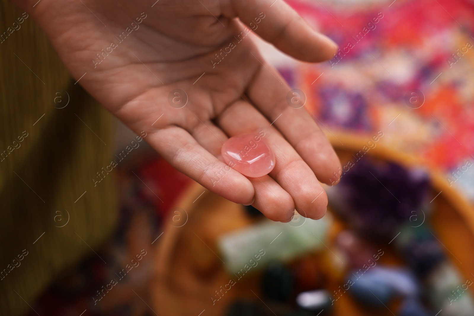 Photo of Woman with beautiful rose quartz indoors, closeup. Natural gemstone