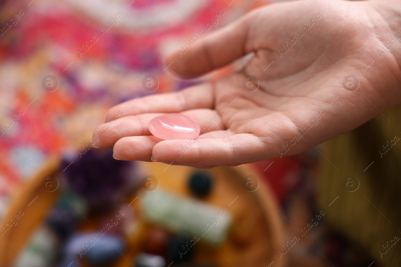 Photo of Woman with beautiful rose quartz indoors, closeup. Natural gemstone