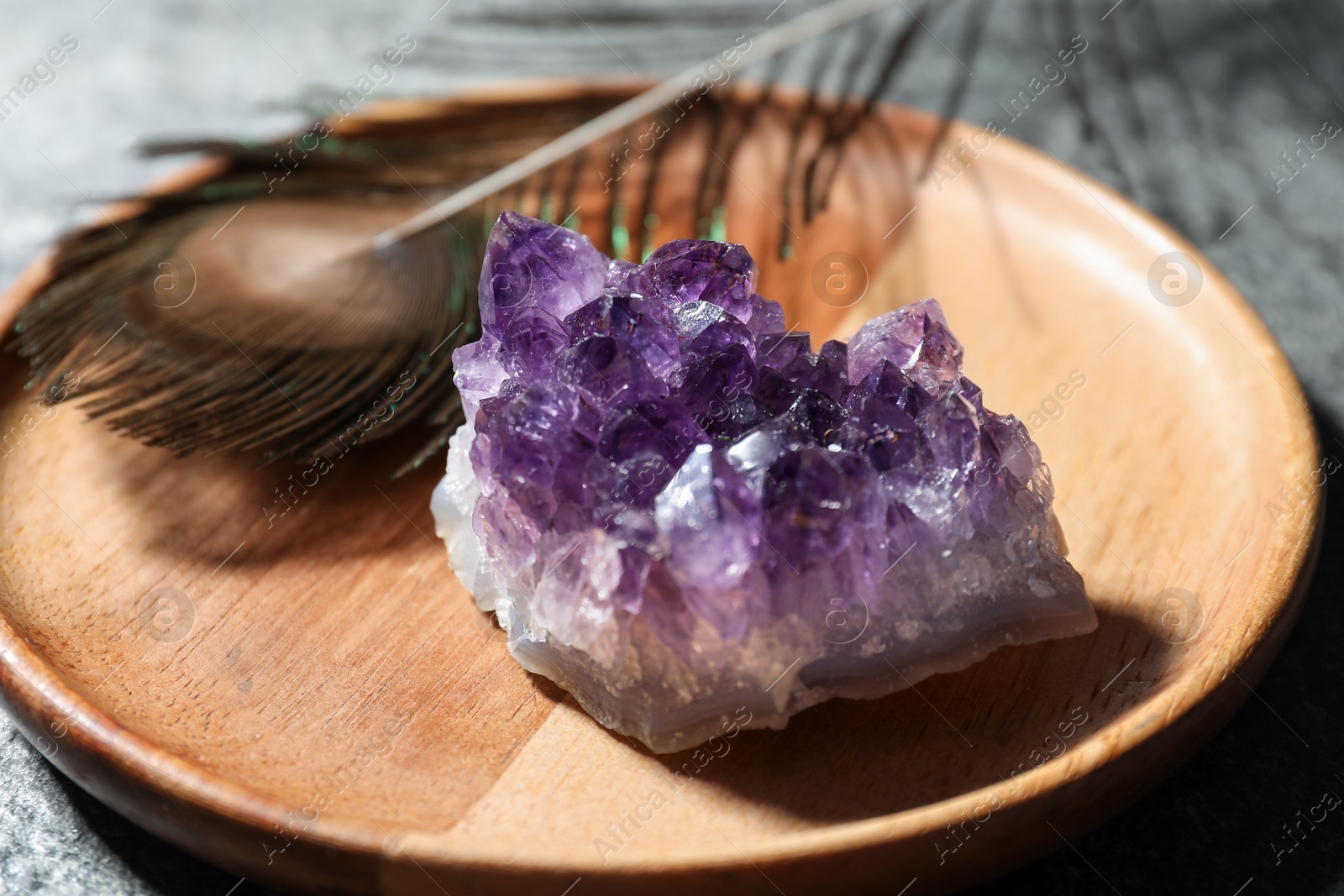 Photo of Beautiful amethyst gemstone and peacock feather on table, closeup