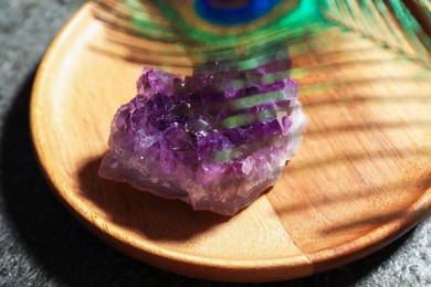 Photo of Beautiful amethyst gemstone and peacock feather on grey table, closeup