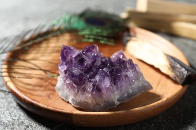 Photo of Beautiful amethyst gemstone, palo santo and peacock feather on grey table, closeup