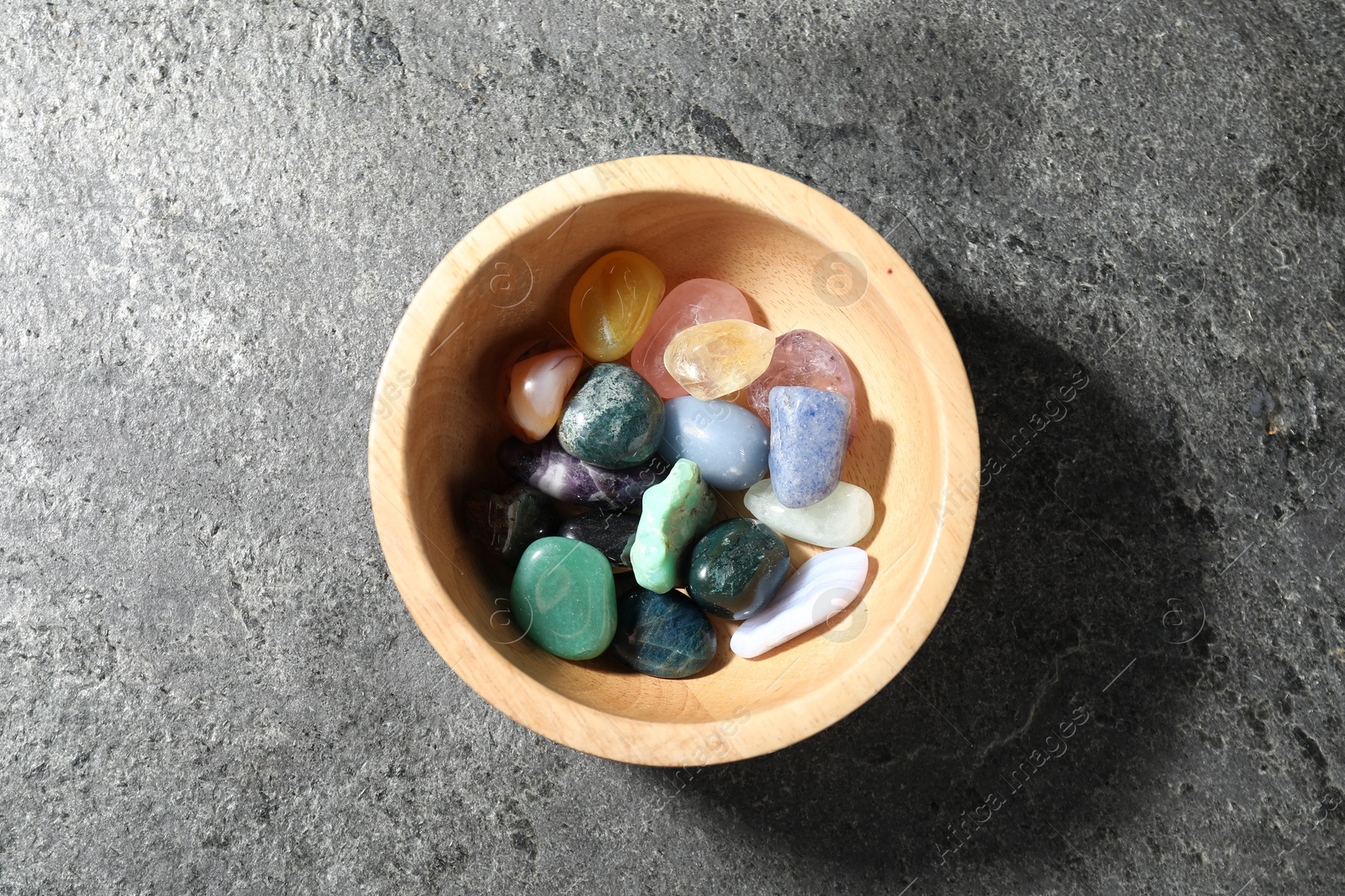 Photo of Different beautiful gemstones in bowl on grey table, top view