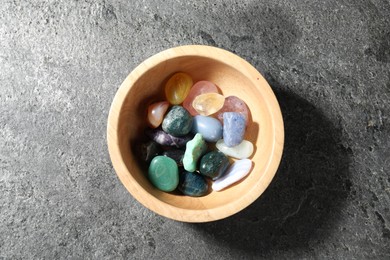 Photo of Different beautiful gemstones in bowl on grey table, top view